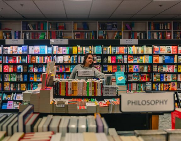 A person reaches for a book inside Unity books, while standing in front of a colourful bookshelf.