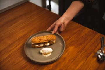 Hand holding plate of dessert, with a dollop of ice cream next to an oval shaped biscuit full of dessert.