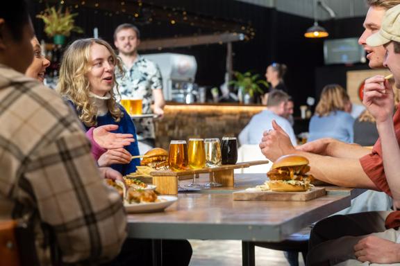 People sitting at a table with beers and burgers at Aro Bar in Brewtown, Upper Hutt. The main focus point is a person talking.