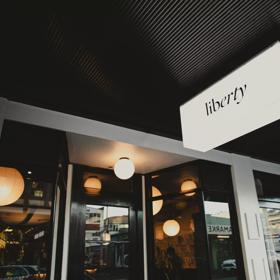 The storefront of Liberty, a restaurant in Te Aro Wellington. It's a white building with black accents and six circular ceiling lights. 