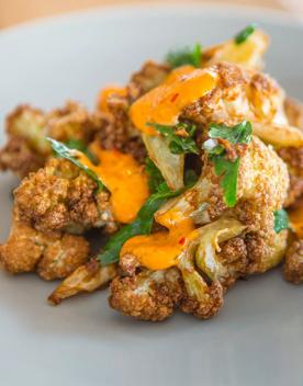 Crispy cauliflower with a drizzle of harissa mayonnaise sits on a light grey plate.