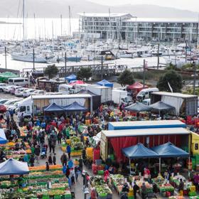 An aerial view of the bustling Habourside Market in Te Aro Wellington. There are tents set up, heaps of colourful produce and many people shopping.