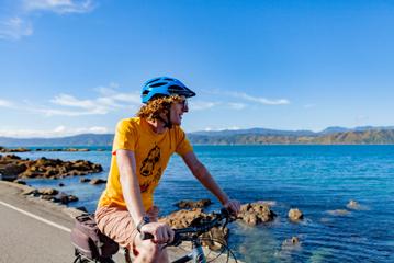 A person wearing yellow biking along Seatoun on an electric bike from Switched On Bikes.