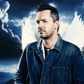 Jim Jefferies with angel wings on a stormy mountain background.