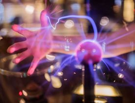 A hand touching a plasma ball with filaments extending between the inner and outer spheres at the Wellington Museum.