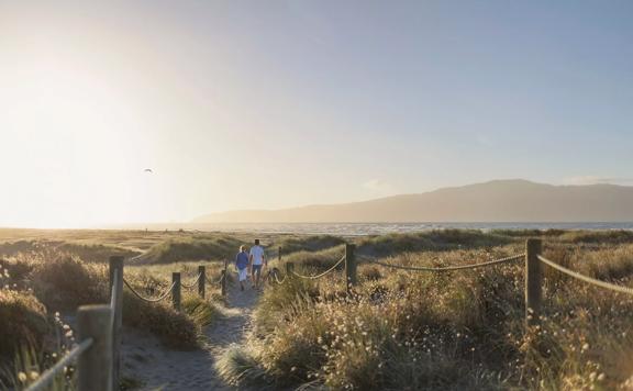 People walking along the sand dune path onto Paraparaumu beach, Kapiti island seen offshore.