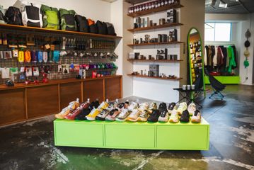 Trail shoes on display at the Coffee Outdoors Wellington store with outdoor equipment including cups, coffee makers and clothing in the background.