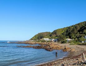 Breaker Bay on a sunny day, blue and green waves crashing on the stoney shore, with green cliffs surrounding.