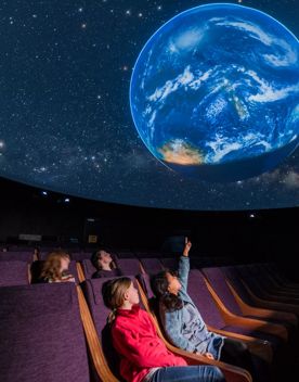 Young children pointing up at the Earth projected onto the digital planetarium and Space Place.