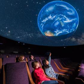 Young children pointing up at the Earth projected onto the digital planetarium and Space Place.