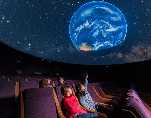 Young children pointing up at the Earth projected onto the digital planetarium and Space Place.