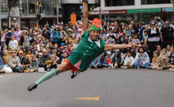 A person in a Christmas elf costume holding on to an acrobat's rope. Their arm and legs are splayed out as they spiral around.