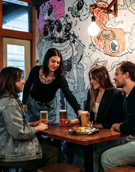 A waiter hands a beer to a table of three inisde Garage Project. The wall behind them is covered in hand drawn art.