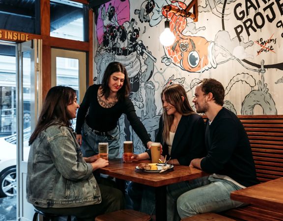 A waiter hands a beer to a table of three inisde Garage Project. The wall behind them is covered in hand drawn art.