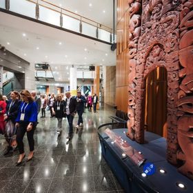 Delegates walk through the Te Papa entrance next to a Māori carving.
