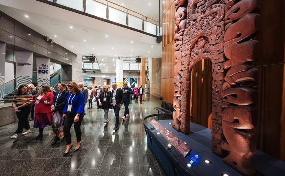Delegates walk through the Te Papa entrance next to a Māori carving.
