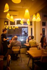 Inside a small restaurant with warm, dim lighting. There are three couples dining and a server taking an order.