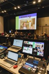 An image taken from behind the tech desk at the New Zealand Game Developers Conference, with laptops and monitor screens projecting onto a large screen in front.