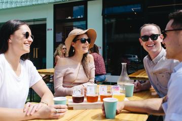 Four friends enjoy a flight of beers on thee patio at Heyday Beer Co on a sunny day.