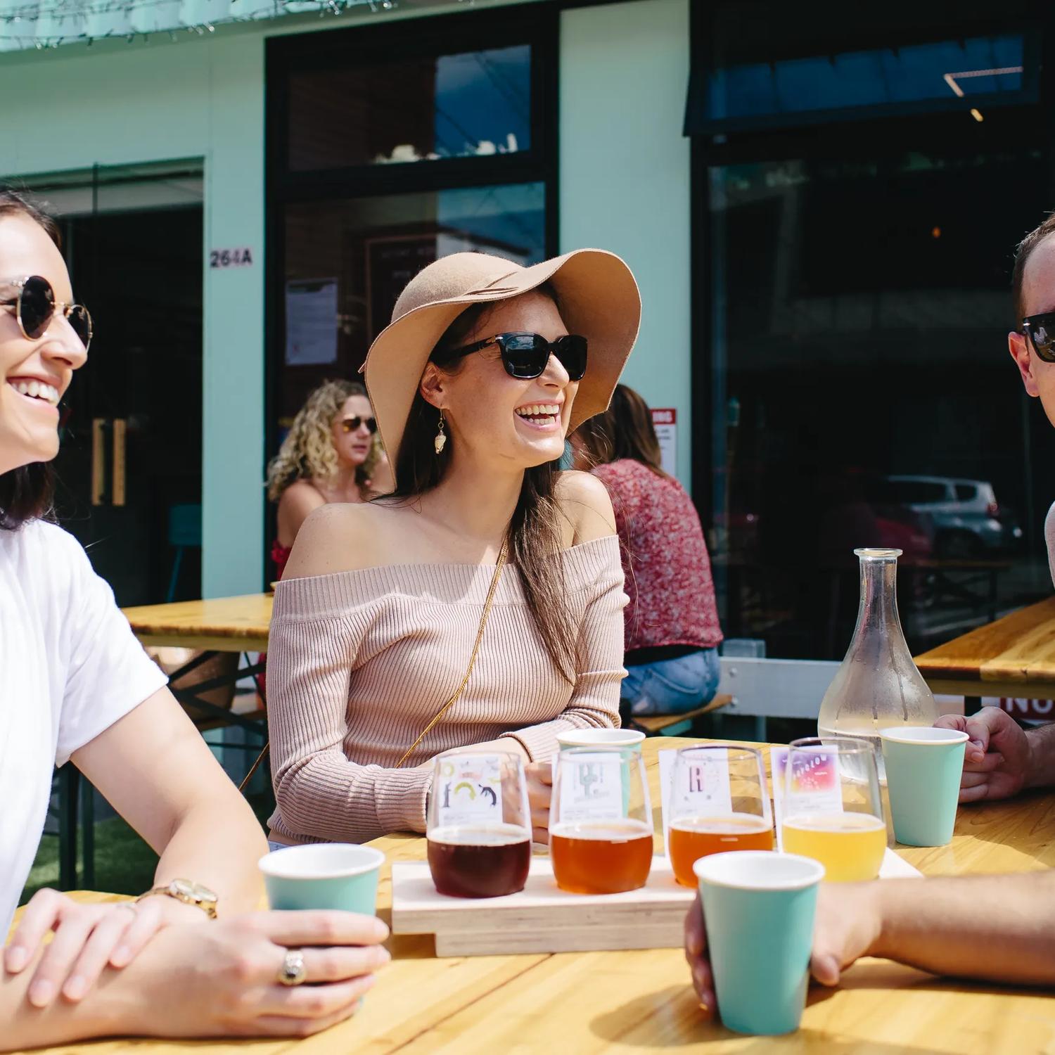 Four friends enjoy a flight of beers on thee patio at Heyday Beer Co on a sunny day.