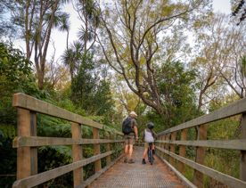 A father and child stand next to each other on a wooden bridge on the Tauwharenikau Trail in the Wairarapa region.