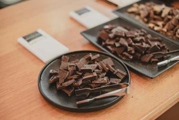 Three plates of chocolate pieces with small silver tongs are to be sampled on a table at the Wellington Chocolate Factory.