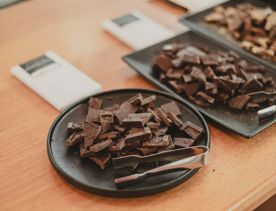 Three plates of chocolate pieces with small silver tongs are to be sampled on a table at the Wellington Chocolate Factory.