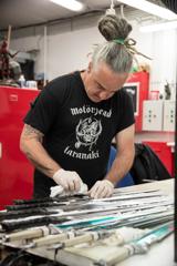 A person wearing a black teeshirt and latex gloves cleans prop swords in a workshop.