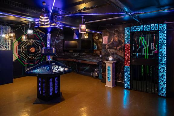 The interior of Escape Mate, an escape room located in Wellington Central. The room has colourful accent lighting and futuristic-space-themed decor. 