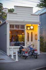 The exterior of Rita in Te Aro valley at sunset with their yellow lighting shining through the glass.