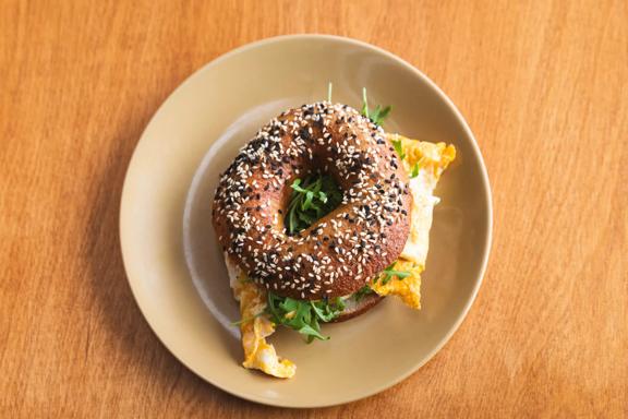 An everything bagel egg sandwich on a beige round plate placed on a wooden surface at Good Boy, a café in Newtown, Wellington.