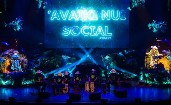 Eight performers on stage at Kia Mau 2025 with a jungle looking backdrop and blue lights shining on them.
