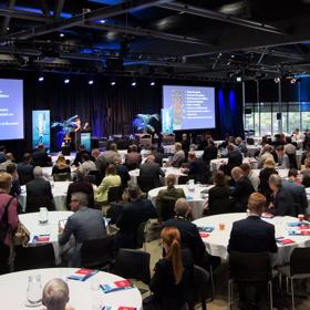 Hundreds of people seated for a conference inside the Lower Hutt Events Centre, looking at 2 large screens to the front of the room.