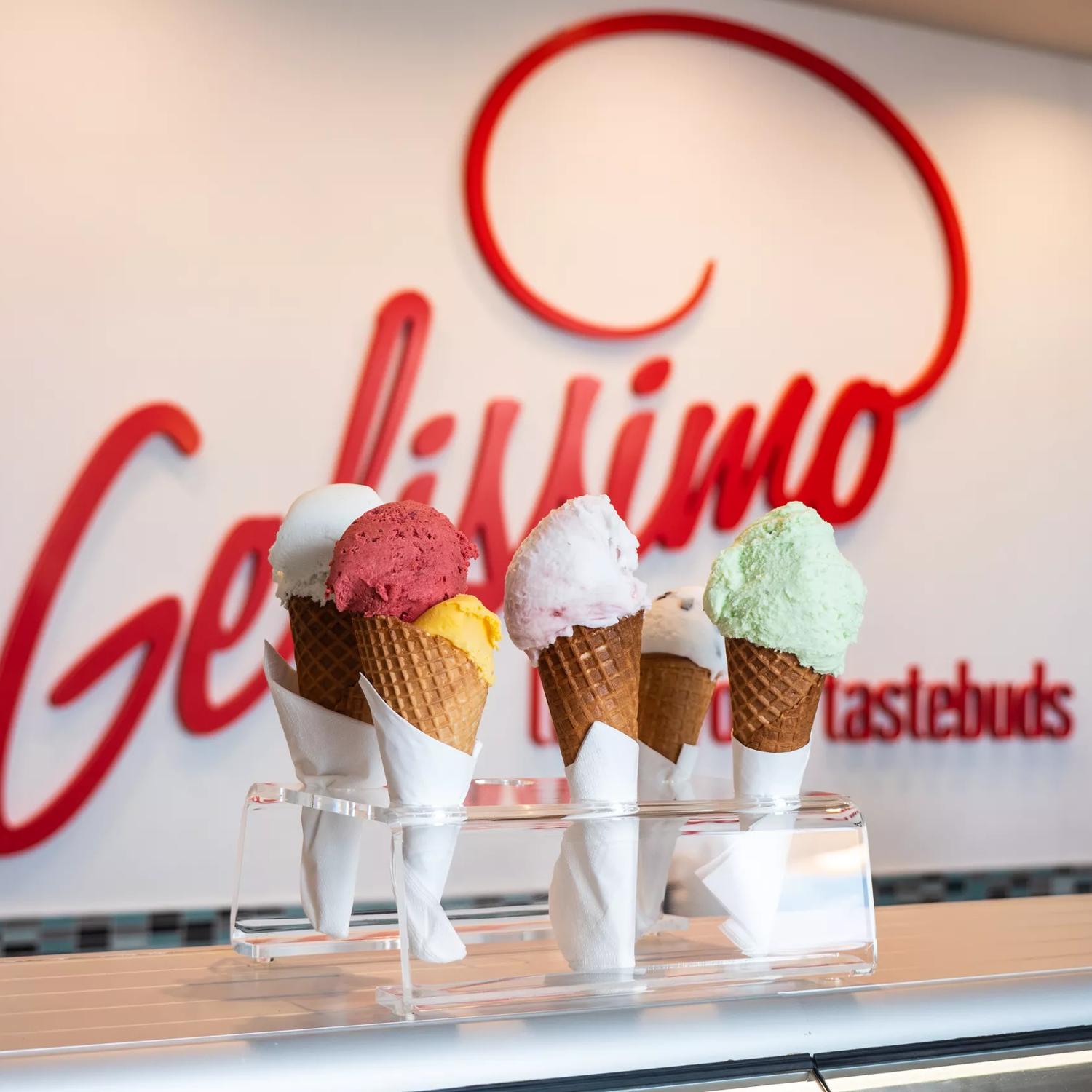 5 different coloured ice creams on a stand in front of the Gelissimo Gelateria sign.