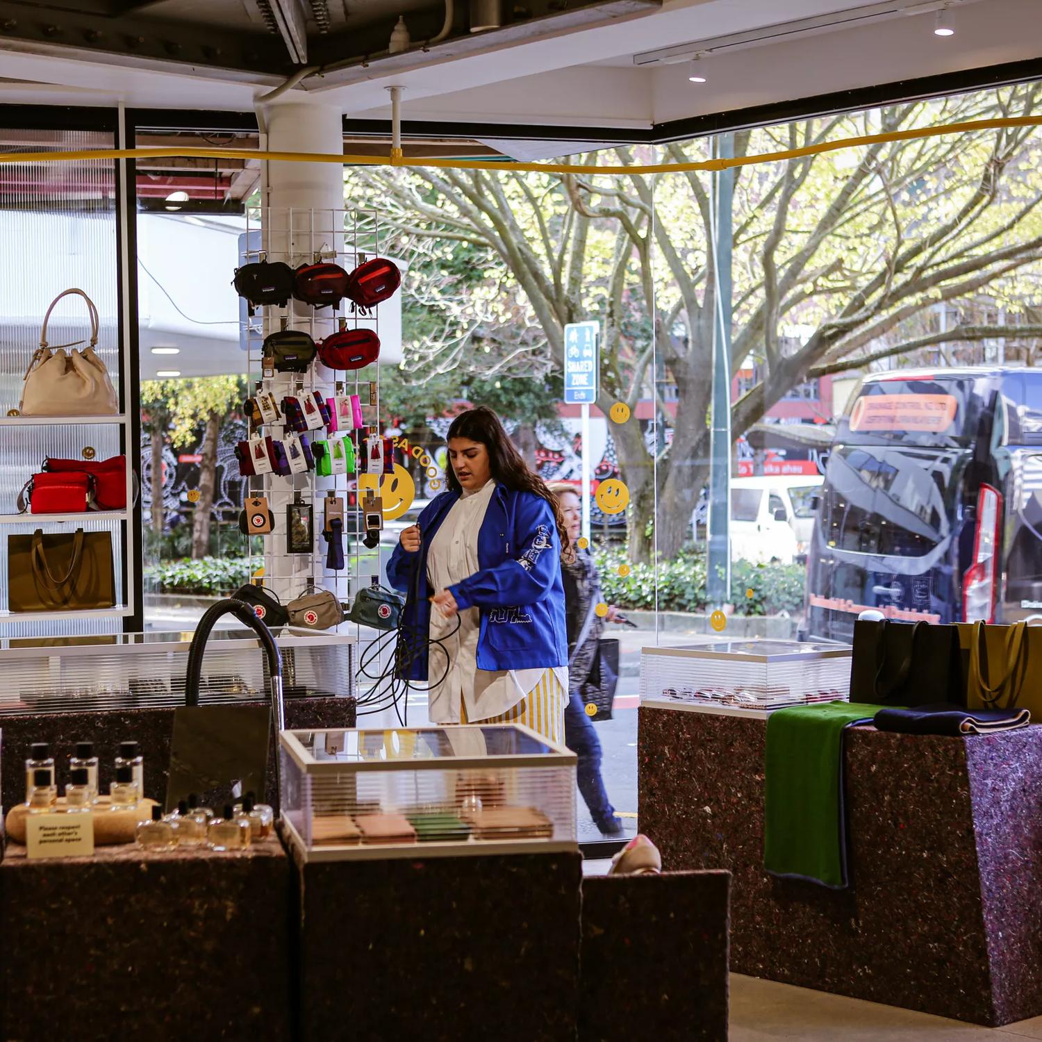 The interior of the shop Good as Gold look out on Bond Street. Glass display cases and shelves hold wallets and bags. The shop assistant stands in the background.