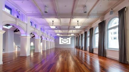 A large room with high vaulted ceilings, arches and pillars along the left, arched windows along the right and hardwood floors. A projection screen on the back wall says "Public Trust Hall".