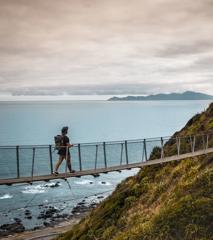 A person wearing a backpack and hat walks along a suspension bridge.