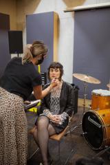 A person sits in a chair while another person applies lipstick on their lips.