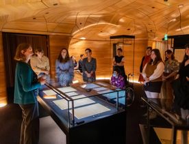 A guide speaks to a group of visitors gathered around display cases containing New Zealand’s founding documents at He Tohu.