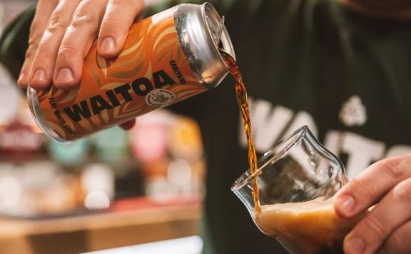 A tall can of Waitoa's 'Earlybird' stout being poured into a glass.