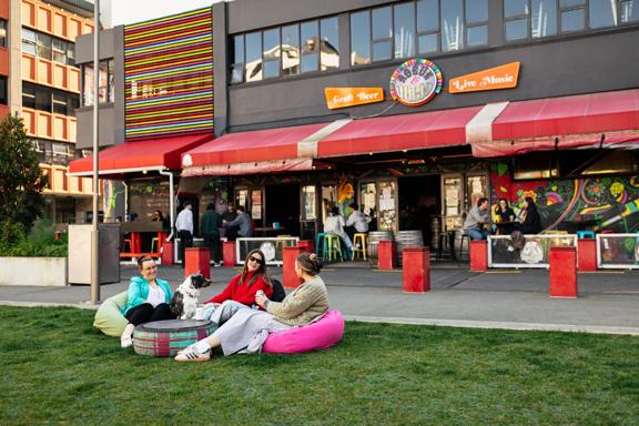 Three friends and a dog sit on bean bag chairs on the grass outside of Rogue and Vagabond.