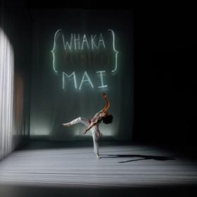 A dancer in a white outfit performs contemporary choreography under a spotlight.