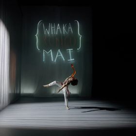 A dancer in a white outfit performs contemporary choreography under a spotlight.