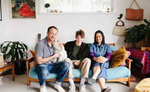 Charlie Faulks (Animator) with Producers Francesca Carney and Ben Powdrell of the web series 'Boke of the Apocolypse' and a scruffy white dog sitting on a living room couch together. 