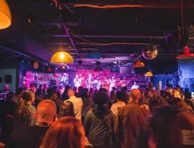A music performance at Meow, a concert venue in Te Aro, Wellington. The stage is lined with bookshelves and the audience is packed with people.