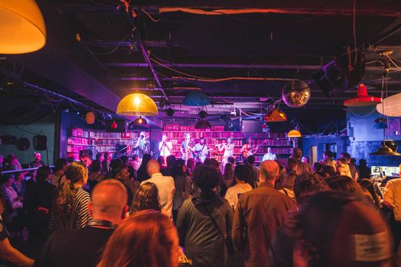 A music performance at Meow, a concert venue in Te Aro, Wellington. The stage is lined with bookshelves and the audience is packed with people.