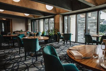 At Bellamy’s three large round wooden tables in a row are set for dinner with green velvet chairs. Smaller tables sit against floor-to-ceiling windows looking out on Parliament.