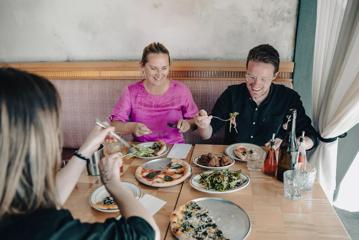 Three people sit at a table enjoying pizza and salad at Scopa, an Italian restaurant on Cuba Street in Te Aro, Wellington.