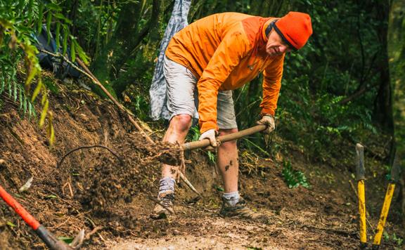 A track-builder shovels dirt on a forest trail.