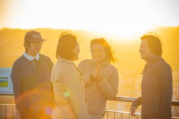 Four friends stand and chat on a sunny windy day at Mount Victoria lookout.